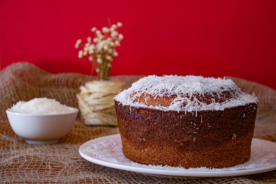 A mouthwatering homemade coconut cake with shredded coconut topping against a vibrant red backdrop.