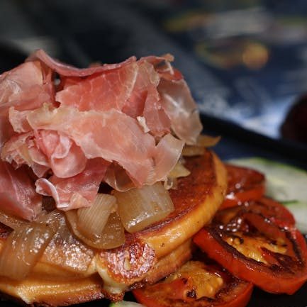 Delicious gourmet breakfast featuring pancakes topped with jamon serrano and roasted vegetables.