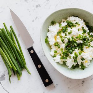 Top view of fresh salad with cottage cheese chopped onion oil and knife fresh greenery on white table with crack