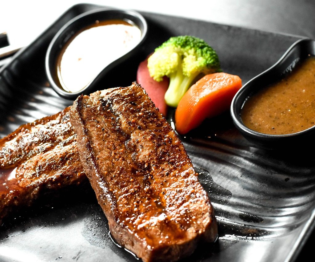 Stek wołowy podany na ciemnym talerzy z sosem pieczeniowym, brokułem i marchewką