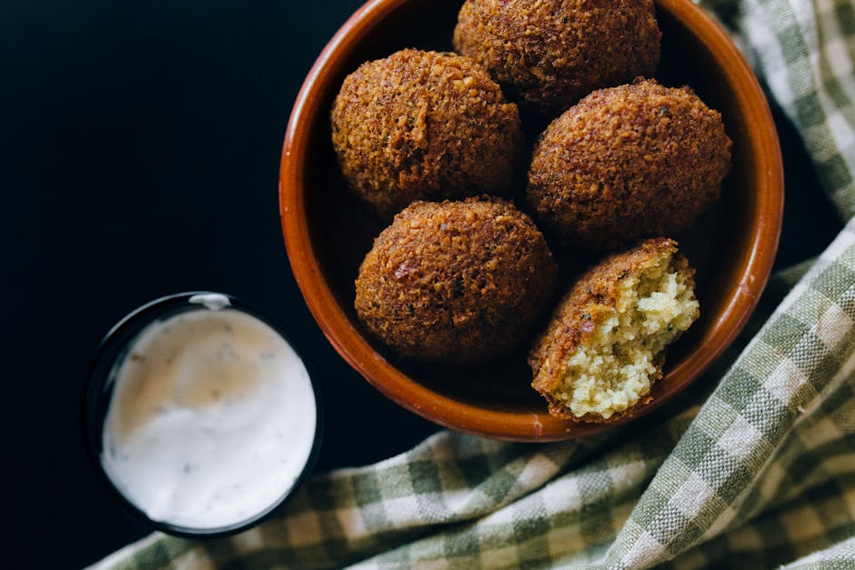 Zbliżenie na chrupiące kulki falafelowe podawane z kremowym sosem tahini w zachęcającym otoczeniu.