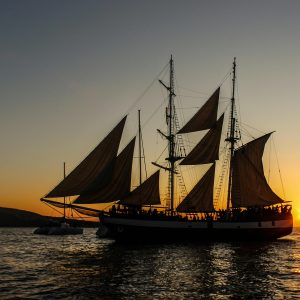 Sylwetka klasycznego żaglowca na tle zachodzącego słońca nad oceanem.