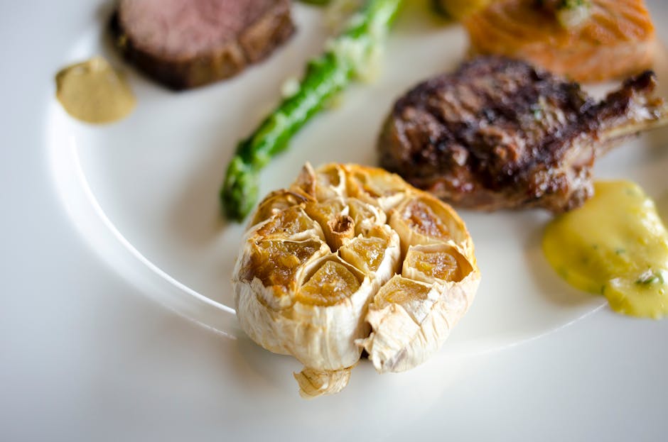 CWykwintne danie z pieczonym czosnkiem i różnymi rodzajami mięsa na białym talerzu.