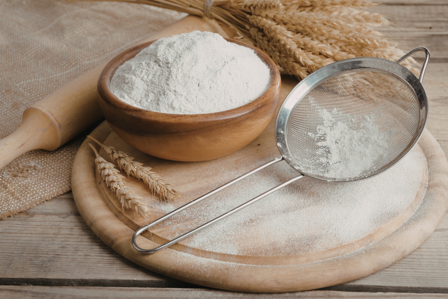 Mąka pszenna w miseczce, obok sitko do przesiewania mąki.